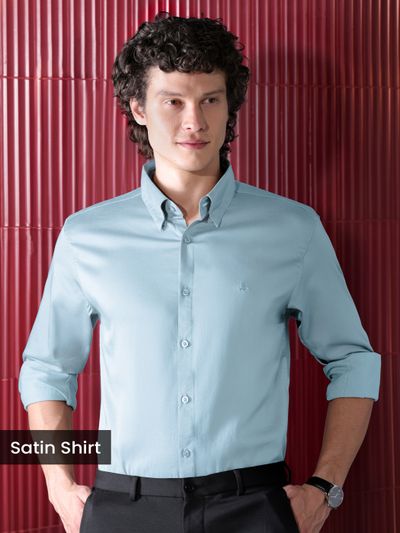 Mens Light Blue Satin Shirt, man sitting on a red leather couch in a stylish, dimly lit setting.