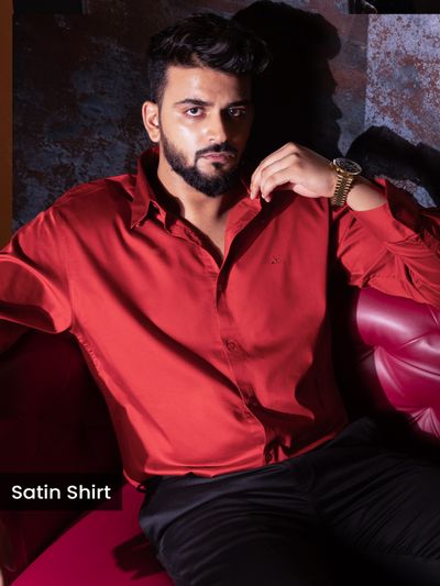 Red Satin Shirt Mens red satin shirt, man sitting on a red leather couch in a stylish, dimly lit setting.